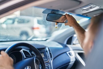 Wall Mural - Young caucasian man touching rearview sitting on car at street