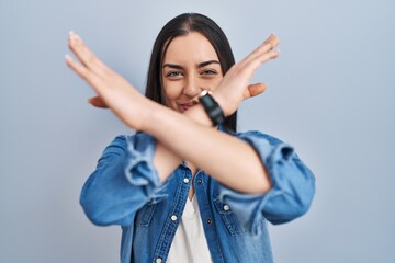 Sticker - Hispanic woman standing over blue background rejection expression crossing arms doing negative sign, angry face