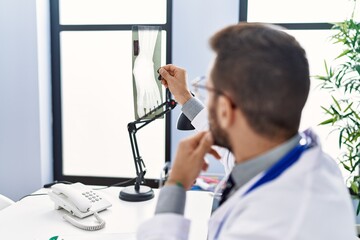 Poster - Young hispanic man wearing doctor uniform looking xray at clinic