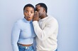 © Krakenimages.com - Young african american couple standing over blue background hand on mouth telling secret rumor, whispering malicious talk conversation
