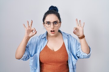 Sticker - Young modern girl with blue hair standing over white background looking surprised and shocked doing ok approval symbol with fingers. crazy expression