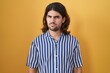 © Krakenimages.com - Hispanic man with long hair standing over yellow background skeptic and nervous, frowning upset because of problem. negative person.