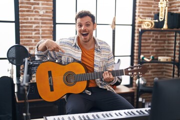 Poster - Young hispanic man playing classic guitar at music studio smiling happy pointing with hand and finger