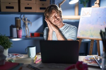 Poster - Middle age man sitting at art studio with laptop at night sleeping tired dreaming and posing with hands together while smiling with closed eyes.