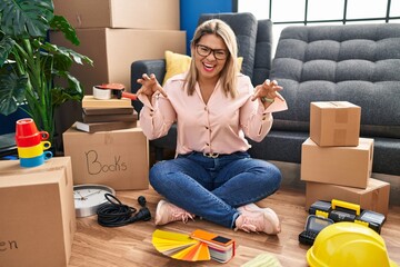 Sticker - Young hispanic woman moving to a new home sitting on the floor smiling funny doing claw gesture as cat, aggressive and sexy expression