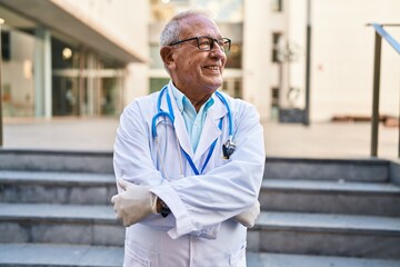 Wall Mural - Senior man wearing doctor uniform standing with arms crossed gesture at street