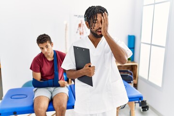 Poster - Young hispanic man working at pain recovery clinic with a man with broken arm yawning tired covering half face, eye and mouth with hand. face hurts in pain.