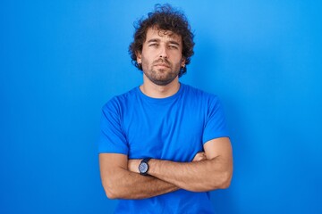 Sticker - Hispanic young man standing over blue background skeptic and nervous, disapproving expression on face with crossed arms. negative person.