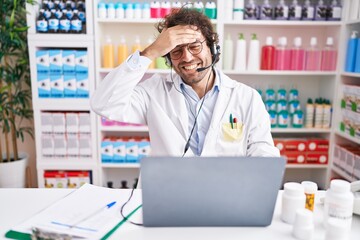 Poster - Hispanic young man working at pharmacy drugstore working with laptop stressed and frustrated with hand on head, surprised and angry face