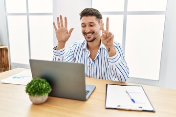 Wall Mural - Young handsome man with beard working at the office using computer laptop showing and pointing up with fingers number seven while smiling confident and happy.