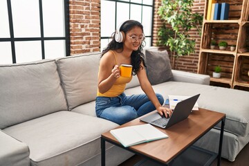 Canvas Print - Young chinese woman listening to music using laptop sitting on sofa at home