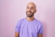 © Krakenimages.com - Middle age bald man standing over pink background looking away to side with smile on face, natural expression. laughing confident.