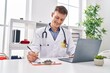 © Krakenimages.com - Young man doctor using laptop writing on clipboard at clinic