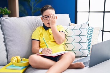 Canvas Print - Young hispanic kid doing homework sitting on the sofa yawning tired covering half face, eye and mouth with hand. face hurts in pain.