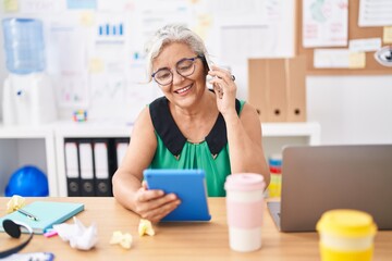 Canvas Print - Middle age grey-haired woman business worker talking on smartphone using touchpad at office