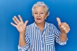 © Krakenimages.com - Senior woman with grey hair standing over blue background showing and pointing up with fingers number six while smiling confident and happy.