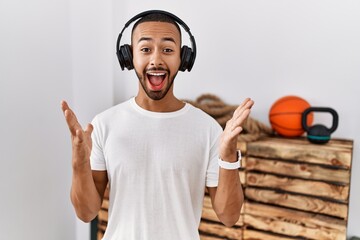 Wall Mural - African american man listening to music using headphones at the gym celebrating crazy and amazed for success with arms raised and open eyes screaming excited. winner concept