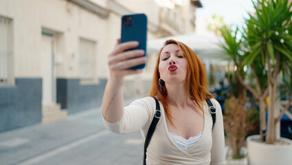 Sticker - Young redhead woman making selfie by the smartphone kissing at street