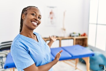 Wall Mural - Black woman with braids working at pain recovery clinic inviting to enter smiling natural with open hand