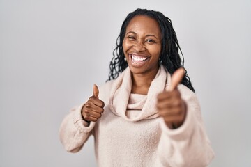 Wall Mural - African woman standing over white background approving doing positive gesture with hand, thumbs up smiling and happy for success. winner gesture.