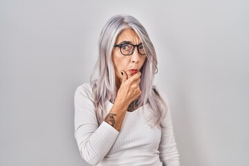 Sticker - Middle age woman with grey hair standing over white background looking fascinated with disbelief, surprise and amazed expression with hands on chin