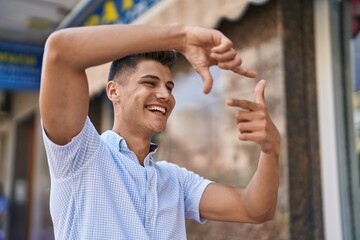 Wall Mural - Young hispanic man smiling confident doing photo gesture with hands at street