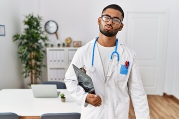 Canvas Print - Young indian man wearing doctor uniform and stethoscope looking at the camera blowing a kiss on air being lovely and sexy. love expression.