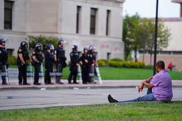 African American sits and watches police in riot gear gather