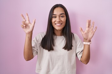 Wall Mural - Young hispanic woman standing over pink background showing and pointing up with fingers number eight while smiling confident and happy.