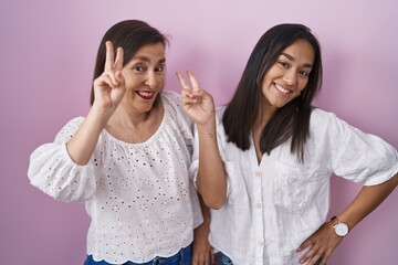 Wall Mural - Hispanic mother and daughter together smiling looking to the camera showing fingers doing victory sign. number two.