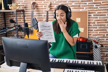 Sticker - Young south asian woman doing online music tutorial showing music sheet covering mouth with hand, shocked and afraid for mistake. surprised expression