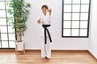 Young hispanic girl wearing karate kimono and black belt approving doing positive gesture with hand, thumbs up smiling and happy for success. winner gesture.