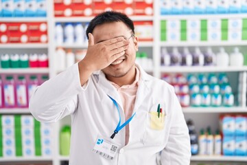 Sticker - Chinese young man working at pharmacy drugstore smiling and laughing with hand on face covering eyes for surprise. blind concept.