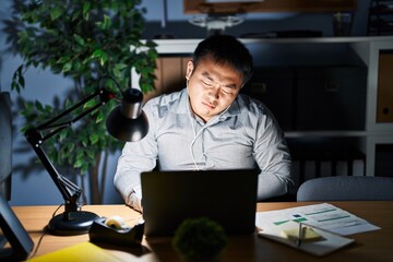 Poster - Young chinese man working using computer laptop at night with hand on stomach because nausea, painful disease feeling unwell. ache concept.