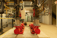 The Interior Of An Old And Well Used Boiler Room With Two Large Mechanical Pumps, Pipes, Valves And Other Equipment.
