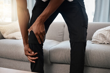 Wall Mural - Black man, hands and knee injury in pain at home from accident, torn muscle or joint ache by living room sofa. African American male suffering from injured leg holding painful area, bruise or bone