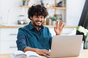 Wall Mural - Young happy Asian man freelancer or entrepreneur have video conference, talking, shows a greeting gesture, working remotely online at home office