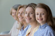 © fizkes - Close up faces in row, diverse women smile looking at camera, little cute girl, her adult mother, mature grandmother and old great-grandmother portraits. Multi-generational family, heredity, offspring