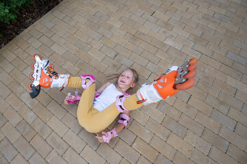 little girl learns to roller skate and falls. view from above