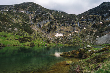 Wall Mural - View on the beautiful blue lake of Ayes, with a waterfall, the pastures and the peaks of the French Pyrenees on a cloudy day in the background