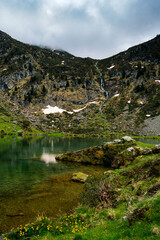 Wall Mural - View on the beautiful blue lake of Ayes, with a waterfall, the pastures and the peaks of the French Pyrenees on a cloudy day in the background