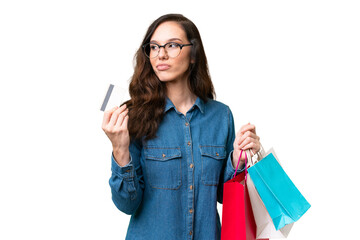 Wall Mural - Young caucasian woman over isolated background holding shopping bags and a credit card and thinking
