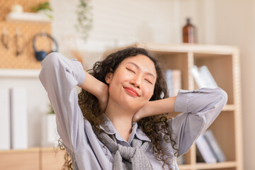 Beautiful Asian young woman close eyes hold on neck and relaxing on chair in living room. Healthy young femal smile take a breath to relax in Calm and quiet place. Comfortable home.