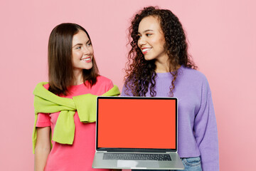 Wall Mural - Young two friends fun IT women in green purple shirts together hold use work on laptop pc computer blank screen workspace area look to each other isolated on pastel plain light pink color background