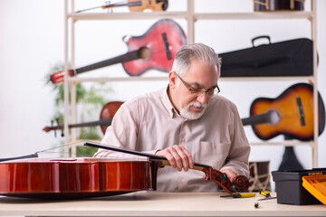 Old male repairman repairing musical instruments at workplace