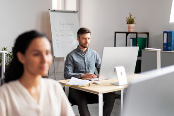 Canvas Print - Serious busy handsome smiling millennial european woman and man managers working at computer