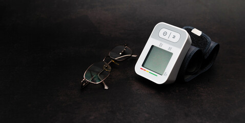 Wall Mural - Automatic digital blood pressure monitor on the wrist, glasses on a black background