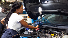 African Female Auto Mechanic Worker Checking Oil Level In Car Engine At Car Service Station. Car Maintenance And Auto Service Garage Concept.