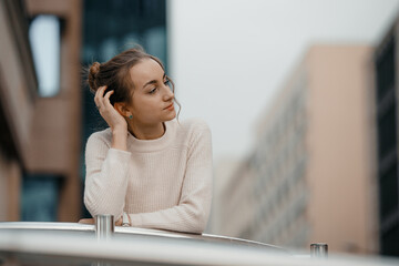 Professional woman worker wear standing outdoor terrace with a smile leaning on railing enjoy view from modern office skyscraper. Tall stylish girl near the railing and steps on the city background.