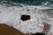 Aerial view of a rock in the shore with splashing sea waves